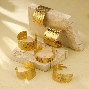 Golden titanium steel open cuff bracelets with various textured patterns on stone background