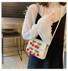 Detail of white woven straw crossbody bag with red cherry pom-poms on black dress