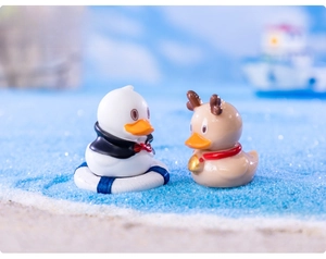 Miniature resin duck figurines with Christmas accessories on blue decorative sand