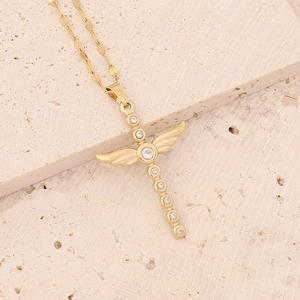 Detail shot of a gold winged cross necklace with zircons on a textured stone surface
