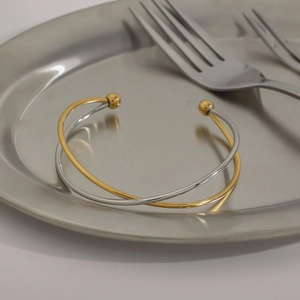 Crossed gold and silver stainless steel open bangle with bead ends on a metal plate