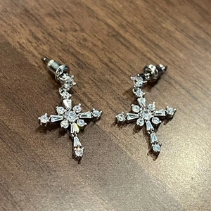 Close-up of silver cross earrings with multiple zircon cuts on a wooden surface