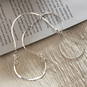 S925 sterling silver bow earrings and snake chain bracelet on aesthetic magazine background