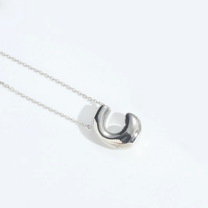 Close-up of a polished silver metal bean pendant on a sleek chain necklace with reflective finish