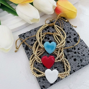 Detalle de tres pulseras con dije de corazón de cristal y cuentas de cobre dorado.
