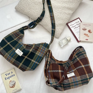 Detail of plaid wool crossbody bags in green and brown on a cozy white sofa setup