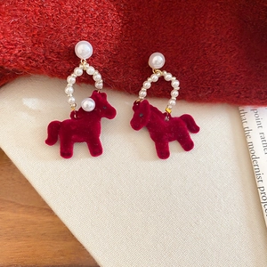 Detailed view of red flocked pony charm and white pearl stud earrings on knit background