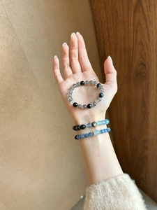 Close-up of moonstone and obsidian beaded bracelets with silver floral spacers on a wrist