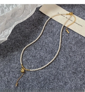 Vue à plat d'un collier de perles avec pendentif gourde dorée et pompons brillants