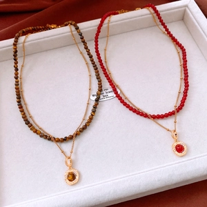 Detail of 18K gold-plated layered necklaces with tiger eye and red stone pendants