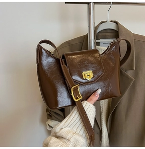 Detailed view of dark brown glossy leather shoulder bag with golden metallic clasp