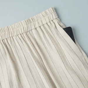 Detail of striped linen-textured pants featuring elastic waist and functional side pocket