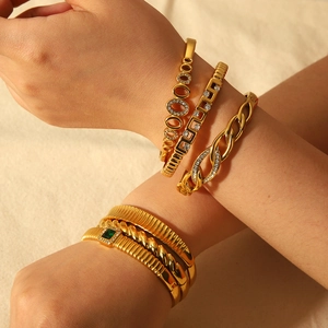 Détail de bracelets superposés en acier doré avec zircons et pierres précieuses vertes
