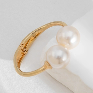 Detailed close-up of a minimalist gold bangle featuring two large white pearls on a stone base
