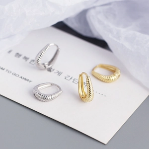 Close-up of gold and silver teardrop twist hoop earrings on a minimalist white display