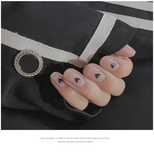 Short oval nude nails with black heart patterns on a stylish black jacket background