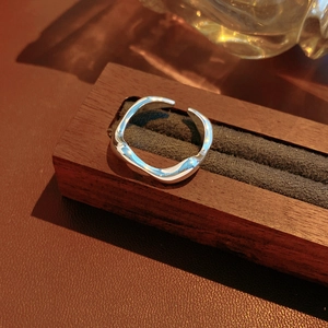 Detailed close-up of wavy irregular open ring with polished silver finish on wood stand