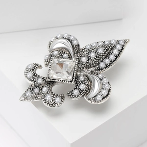Détail macro d'une broche fleur de lys argentée avec perles et une gemme carrée centrale