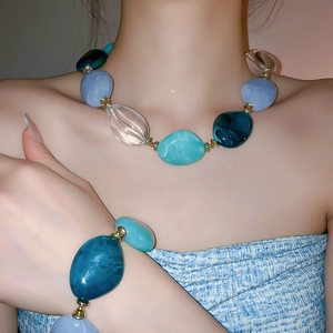 Detail view of acrylic oval beaded necklace and bracelet set in blue and teal tones