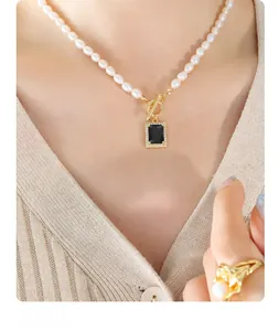Detailed close-up of a gold OT clasp pearl necklace with a black zircon pendant on a model