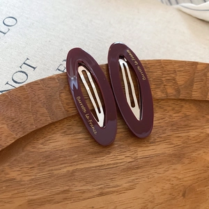 Close-up of oval burgundy acetate hair clips with gold lettering on a wooden tray