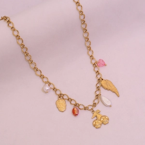 Détail d'un collier doré avec pendentifs tête de mort, cœur et cerises sur fond rose