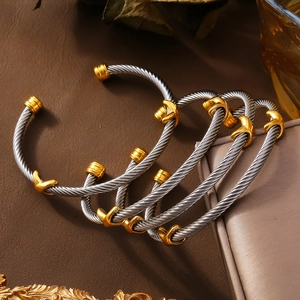 Stacked silver and gold twisted cable cuff bracelets on a textured leather surface