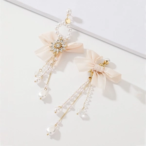 Detail of bow earrings with imitation pearls, rhinestones, and tassel chains on white background