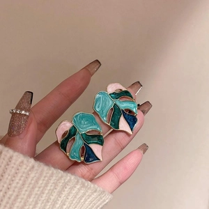Detailed close-up of monstera leaf earrings with colorful enamel and gold-plated edges