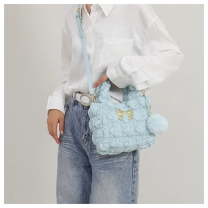 Close-up of light blue quilted cloud bag featuring a gold bow and soft pompom charm