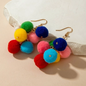 Macro shot of colorful woven pompom earrings on a white stone background for Christmas