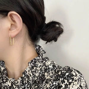 Close-up of minimalist gold square geometric earrings worn on ear with clean white background