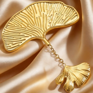 Macro shot of gold ginkgo leaf brooch with realistic veins on champagne satin fabric