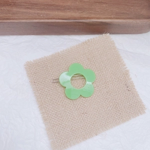 Detail of single green flower hair clip on rustic linen mat with natural studio lighting