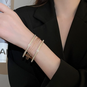 Detail of multi-layered gold bracelet with glitter finish worn on a wrist against black suit