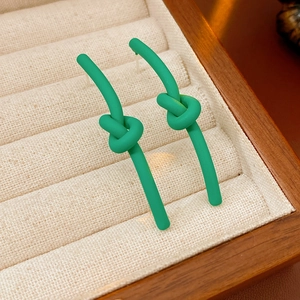 Macro shot of green knotted stud earrings with matte finish in a beige jewelry box
