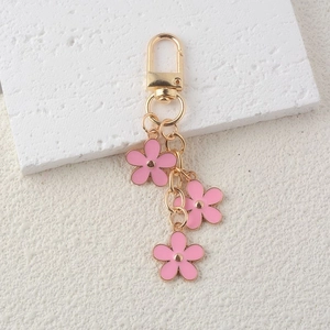 Detailed view of gold keychain featuring three pink alloy flower charms on stone surface