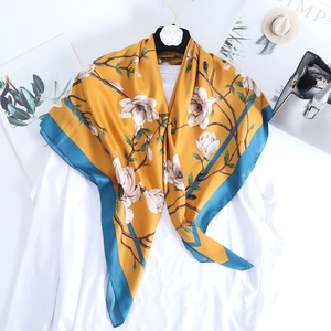 Elegant yellow silk scarf with magnolia floral print draped on a white shirt and hanger