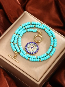 Macro detail of turquoise beaded necklace with golden rhinestone pendant on silk