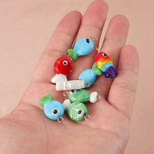 Handheld display of seven colorful handmade glass fish pendants for DIY jewelry making