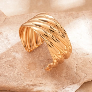 Detailed view of wide golden cuff bracelet with wavy metallic texture on natural stone