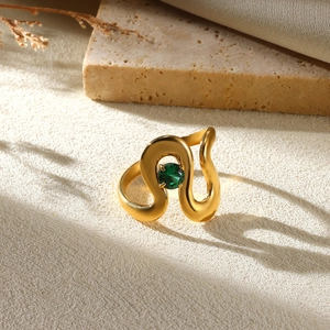 Detailed close-up of a wavy gold ring with a polished green gemstone on a stone surface