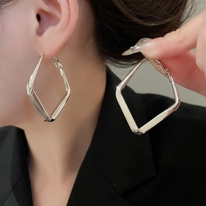 Close-up of geometric diamond-shaped silver drop earrings on model showcasing metallic luster