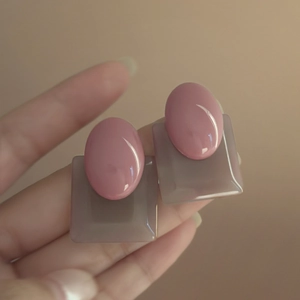 Macro detail of geometric resin earrings in pink and purple held by hand
