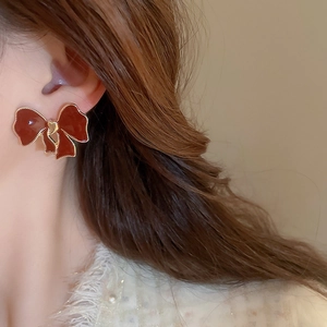 Close-up of vintage red bow earrings with gold trim worn by a model in warm light