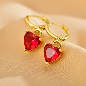 Elegant gold hoop earrings with red heart shaped zircon pendants on beige fabric