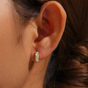 Close-up of golden huggie hoop earring with sparkling micro-diamonds on model's ear