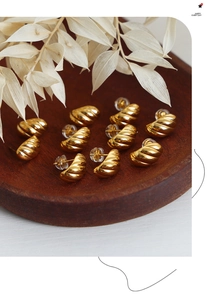 Detailed view of gold-plated twisted C-shaped earrings with silicone backings on wood