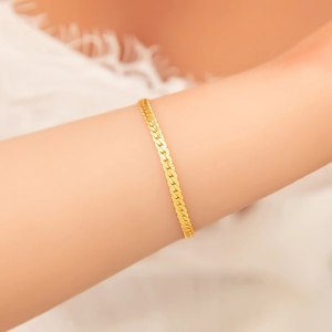 Macro view of gold snake bone chain bracelet showing flat blade texture on woman wrist