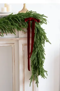 Detail of green PE Christmas garland with a large burgundy velvet bow on a white fireplace